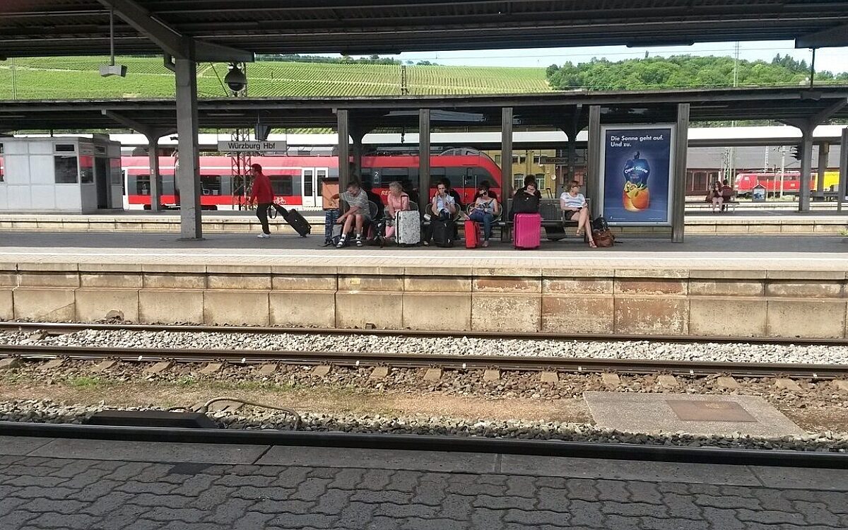 Menschen sitzen mit Gepäck am Würzburger Bahnsteig Bahnhof Menschen sitzen mit Gepäck am Würzburger Bahnsteig Bahnhof