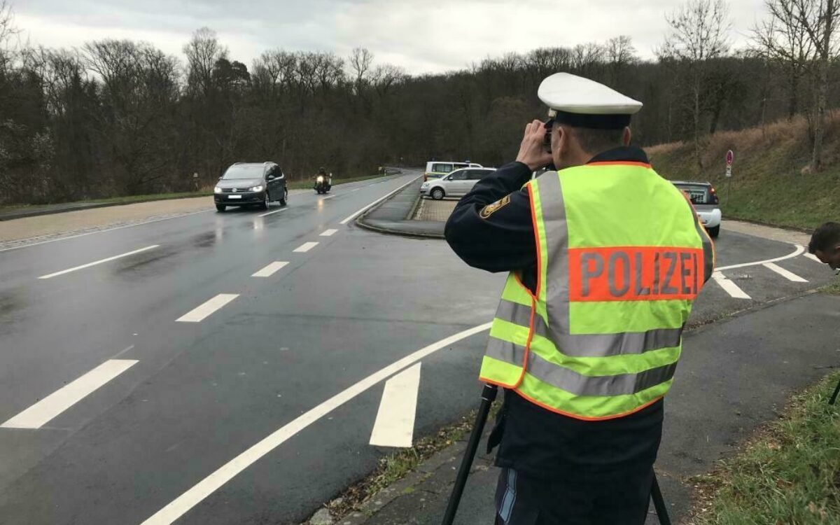 Ein Polizist misst mit der Laserpistole die Geschwindigkeit eines vorbeifahrenden Autos Ein Polizist misst mit der Laserpistole die Geschwindigkeit eines vorbeifahrenden Autos
