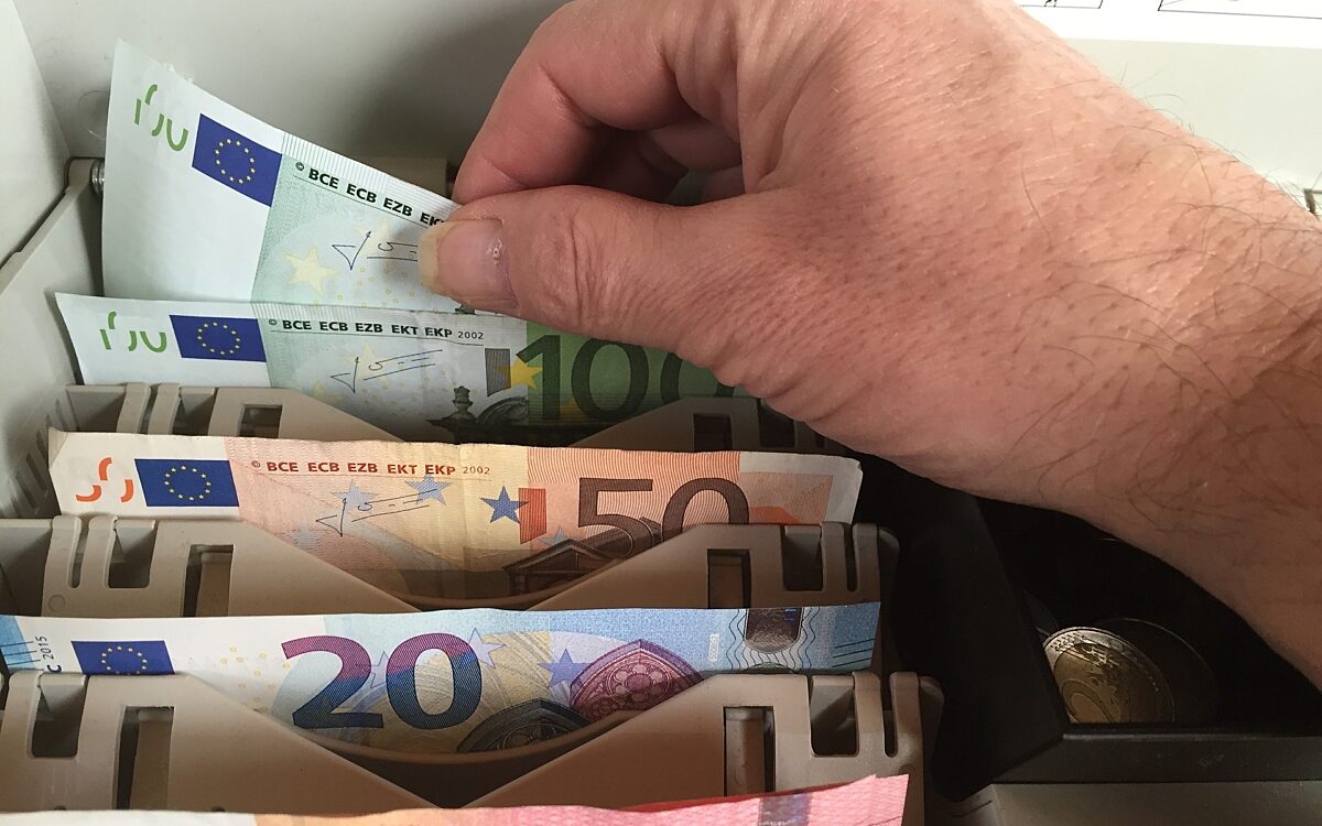 Eine Hand nimmt Geldscheine aus einer Kasse Eine Hand nimmt Geldscheine aus einer Kasse