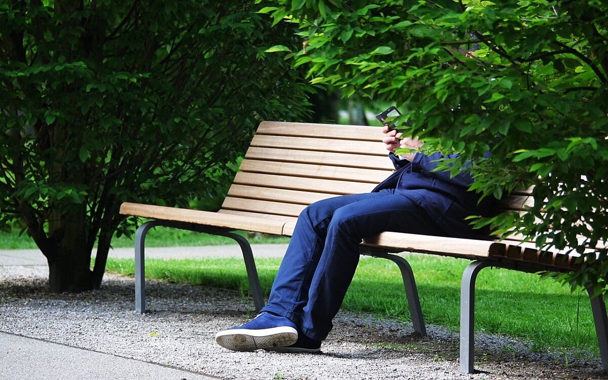 Mann sitzt auf einer Parkbank Mann sitzt auf einer Parkbank