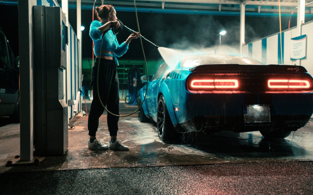 Eine Frau spritzt ein Auto in einer SB-Waschanlage mit einem Hochdruckreiniger ab Eine Frau spritzt ein Auto in einer SB-Waschanlage mit einem Hochdruckreiniger ab
