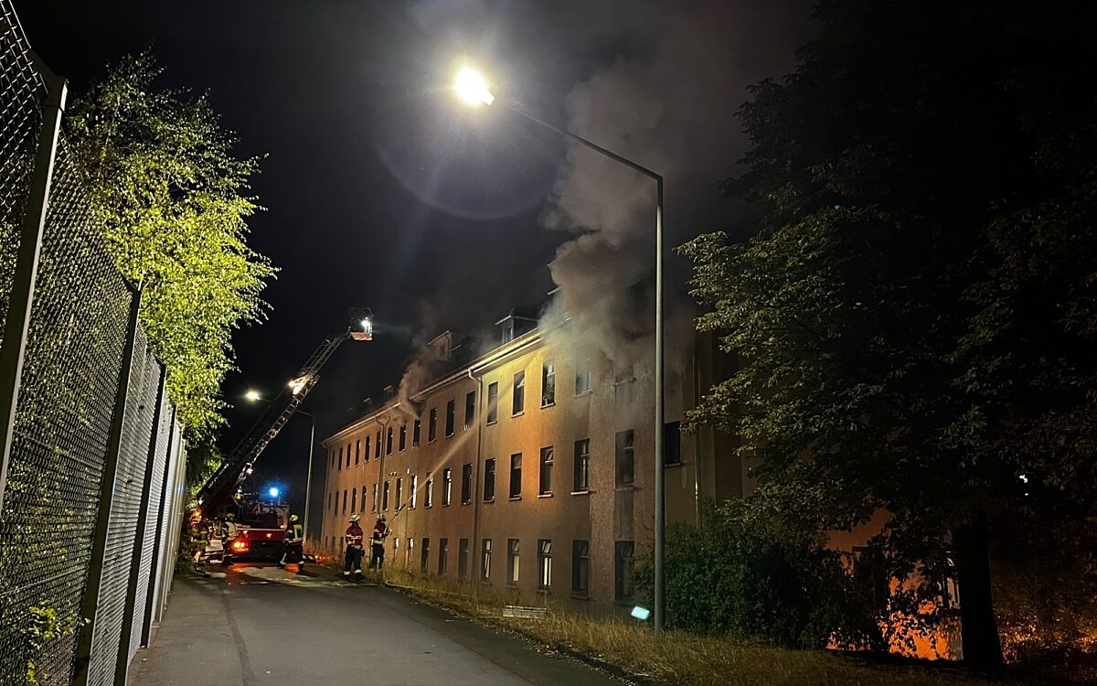 Ein Leiterwagen der Feuerwehr steht vor der Asylunterkunft. Aus einem Fenster dringt Rauch Ein Leiterwagen der Feuerwehr steht vor der Asylunterkunft. Aus einem Fenster dringt Rauch