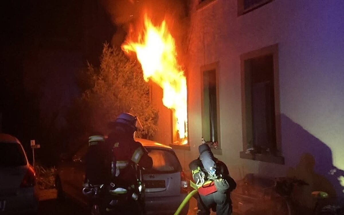 Feuerwehrleute kämpfen sich an die Flammen heran, die aus einem Fenster schlagen