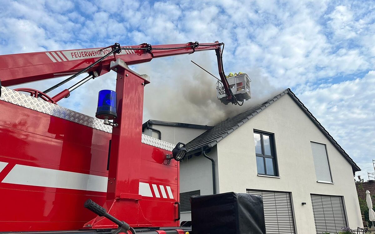 Eine Hubbühne der Feuerwehr steht über den qualmenden Dach eines Wohnhauses Eine Hubbühne der Feuerwehr steht über den qualmenden Dach eines Wohnhauses
