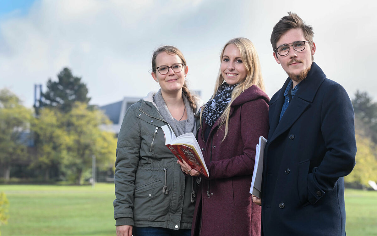 Drei studenten mit einem buch auf dem campus der uni Drei studenten mit einem buch auf dem campus der uni