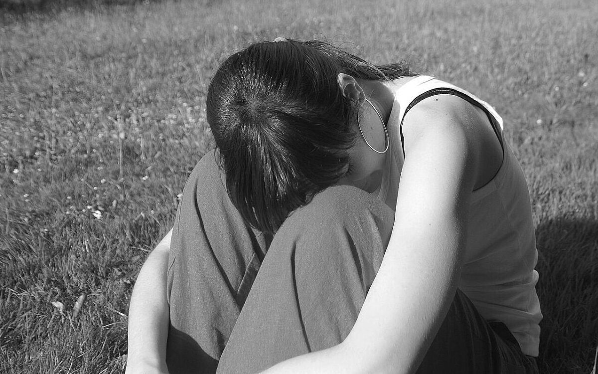 Eine junge Frau sitzt verzweifelt auf einer Wiese Eine junge Frau sitzt verzweifelt auf einer Wiese