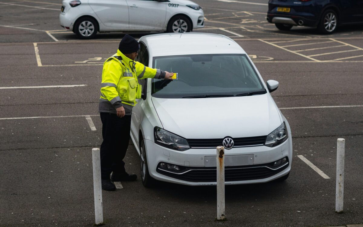 Ein Parkwächter hängt einen Strafzettel an ein geparktes Auto Ein Parkwächter hängt einen Strafzettel an ein geparktes Auto