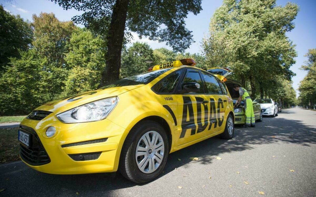 Gelbes ADAC Auto, im Hintergrund Pannenhelfer, der Auto mit geöffneter Motorhaube repariert Gelbes ADAC Auto, im Hintergrund Pannenhelfer, der Auto mit geöffneter Motorhaube repariert