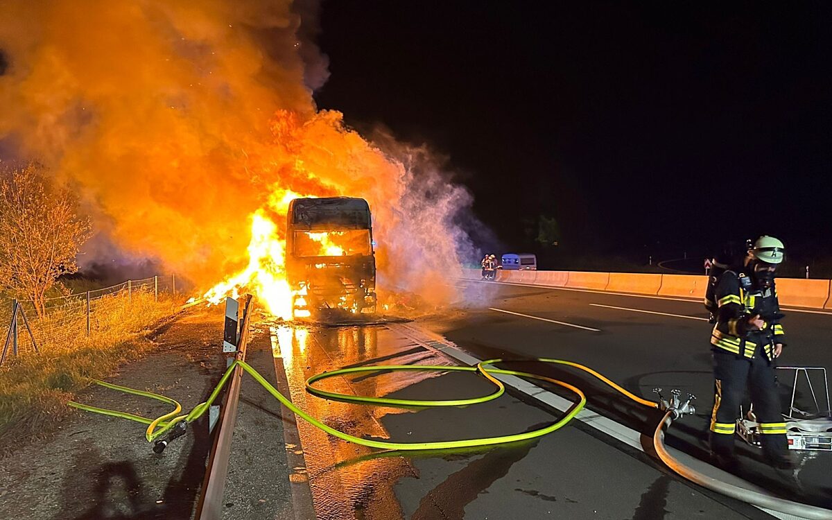 Ein Feuerwehrmann mit Schlauch steht vor einem lichterloh brennenden LKW Ein Feuerwehrmann mit Schlauch steht vor einem lichterloh brennenden LKW