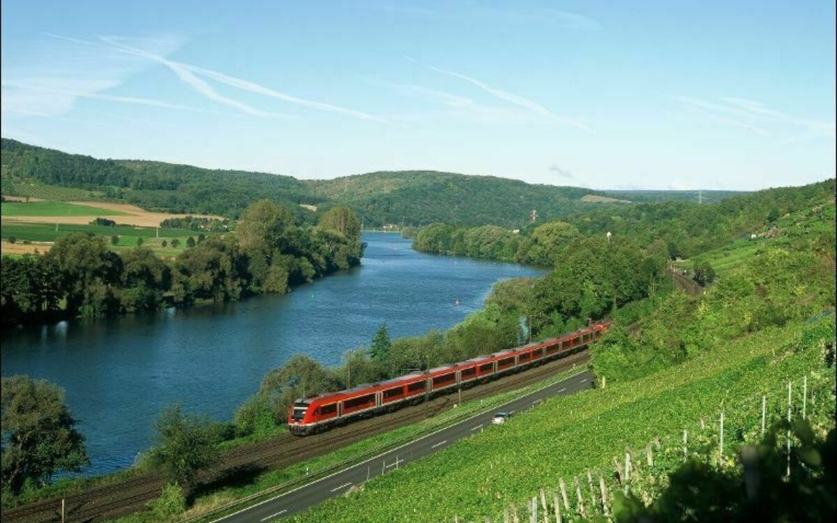 Die rote Main-Spessart-Bahn fährt am Main entlang, ringsherum grüne Bäume, Felder und Weinberge Die rote Main-Spessart-Bahn fährt am Main entlang, ringsherum grüne Bäume, Felder und Weinberge
