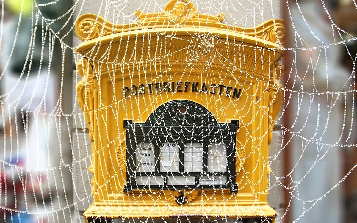 Ein gelber Postbriefkasten. Im Vordergrund hängt ein Spinnennetz Ein gelber Postbriefkasten. Im Vordergrund hängt ein Spinnennetz
