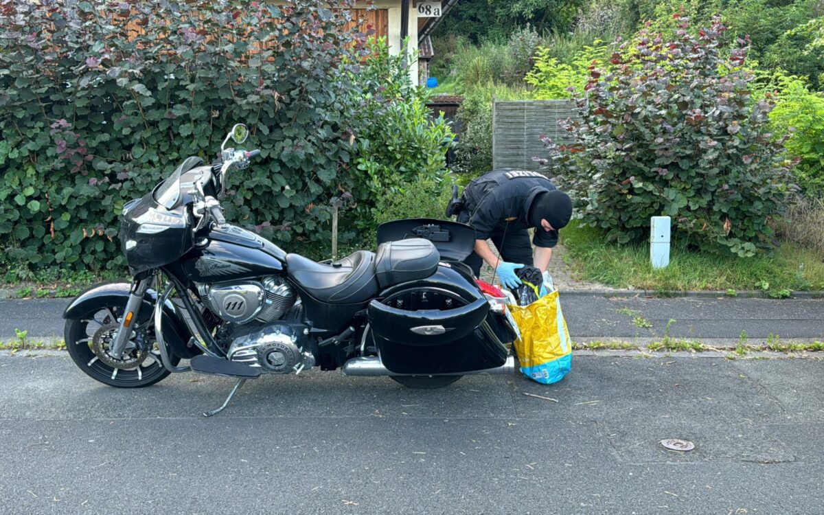 Ein Polizist sammelt Sachen in einer Tüte. Daneben steht ein Motorrad Ein Polizist sammelt Sachen in einer Tüte. Daneben steht ein Motorrad