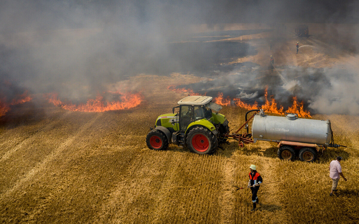 Ein Traktor mit Tankanhänger steht auf einem brennenden Feld um es zu löschen Ein Traktor mit Tankanhänger steht auf einem brennenden Feld um es zu löschen
