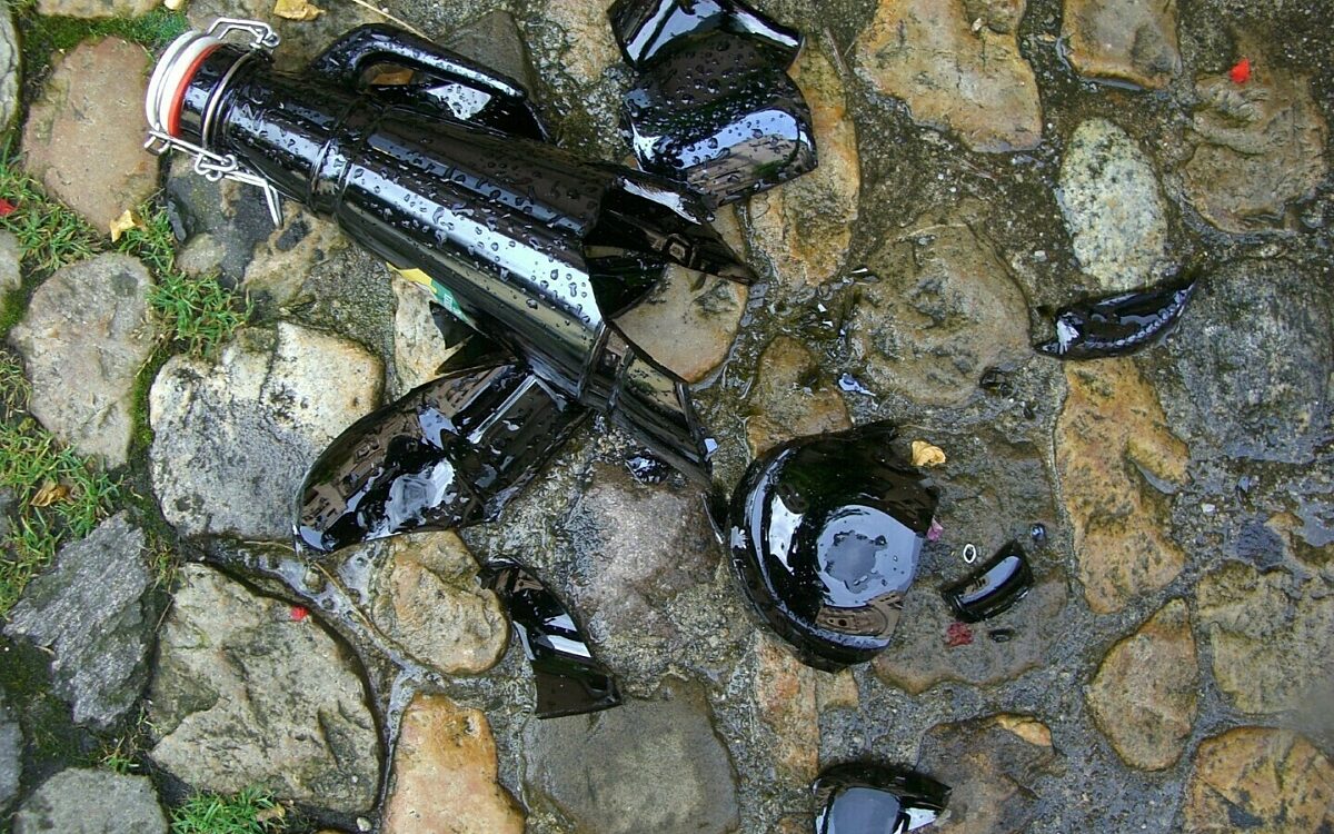 Eine zerbrochene Bierflasche und Scherben am Boden Eine zerbrochene Bierflasche und Scherben am Boden