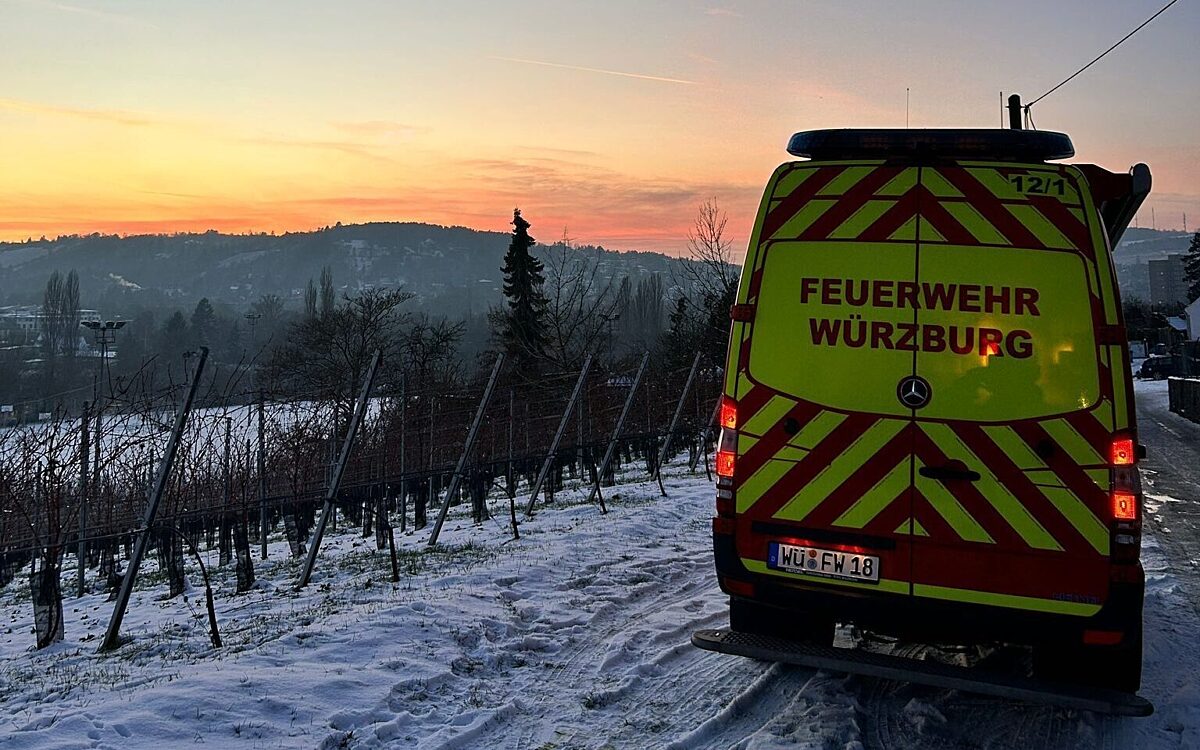 Ein Feuerwehrautos steht auf einem verschneiten Weinbergweg. Im Hintergrund geht die Sonne unter Ein Feuerwehrautos steht auf einem verschneiten Weinbergweg. Im Hintergrund geht die Sonne unter