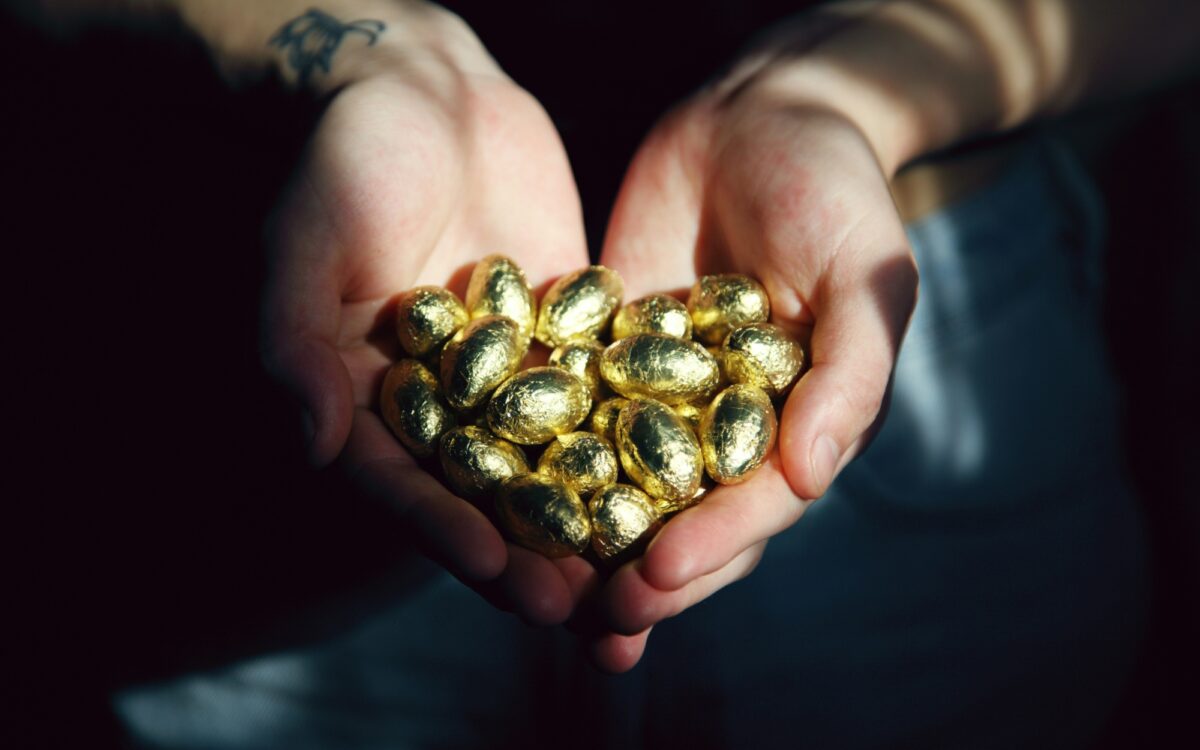 Zwei Hände halten eine Menge golden verpackter Schokoostereier Zwei Hände halten eine Menge golden verpackter Schokoostereier