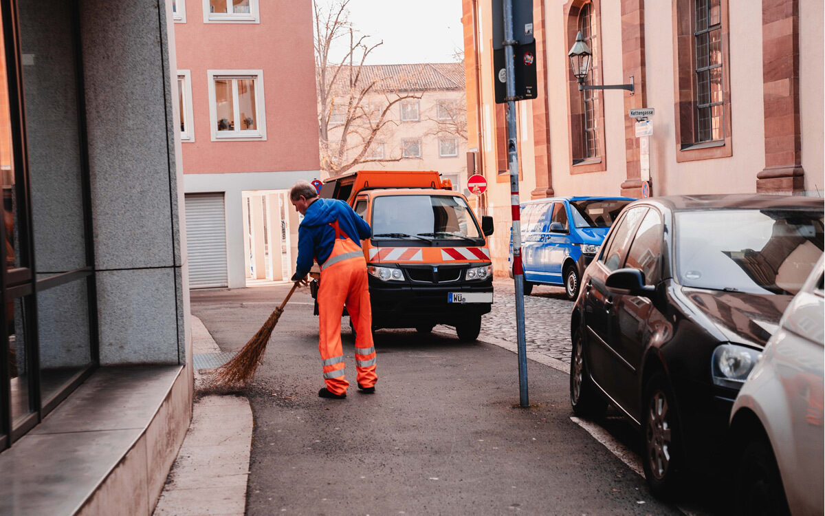 Ein Stadtreiniger ist in Würzburg in der Domerschulstraße am Kehren mit seinem Besen Ein Stadtreiniger ist in Würzburg in der Domerschulstraße am Kehren mit seinem Besen