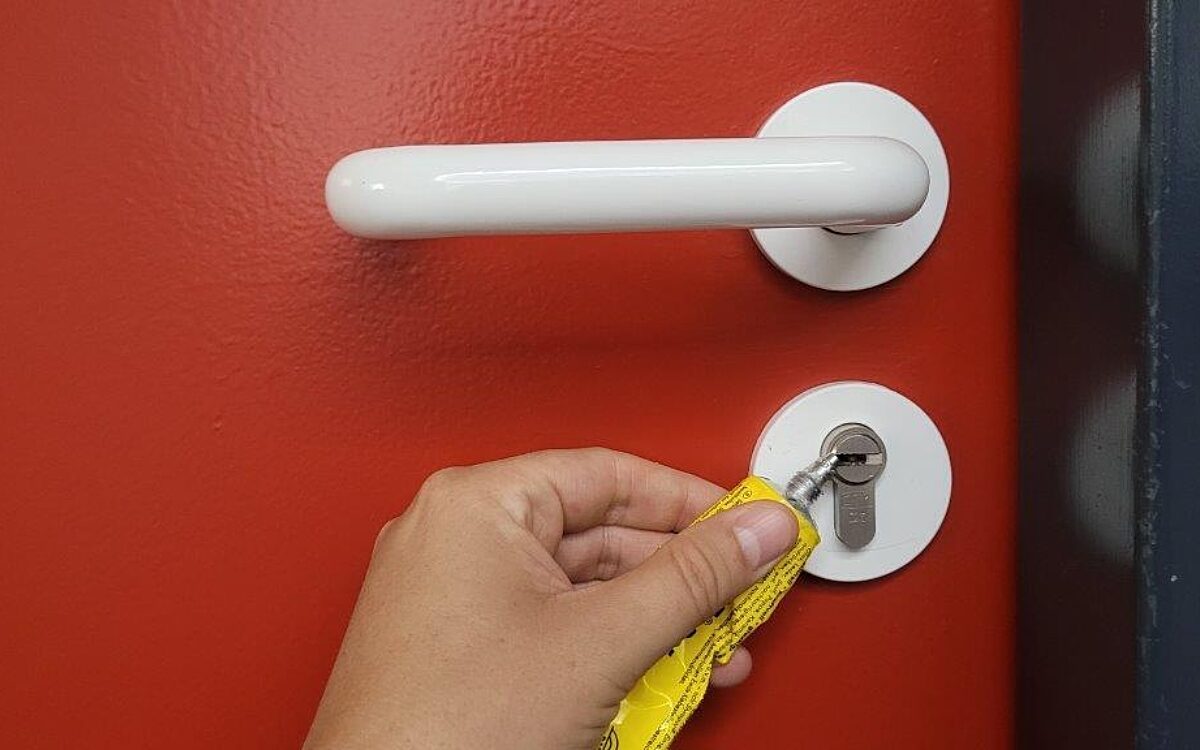 Eine Hand hält eine Tube Kleber um ein Türschloss zuzukleben Eine Hand hält eine Tube Kleber um ein Türschloss zuzukleben